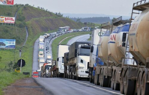 Foto de caminhões em fila em rodovia.