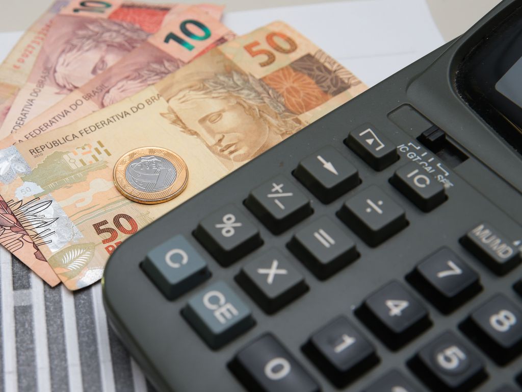Foto de notas de real e uma moeda ao lado de calculadora.