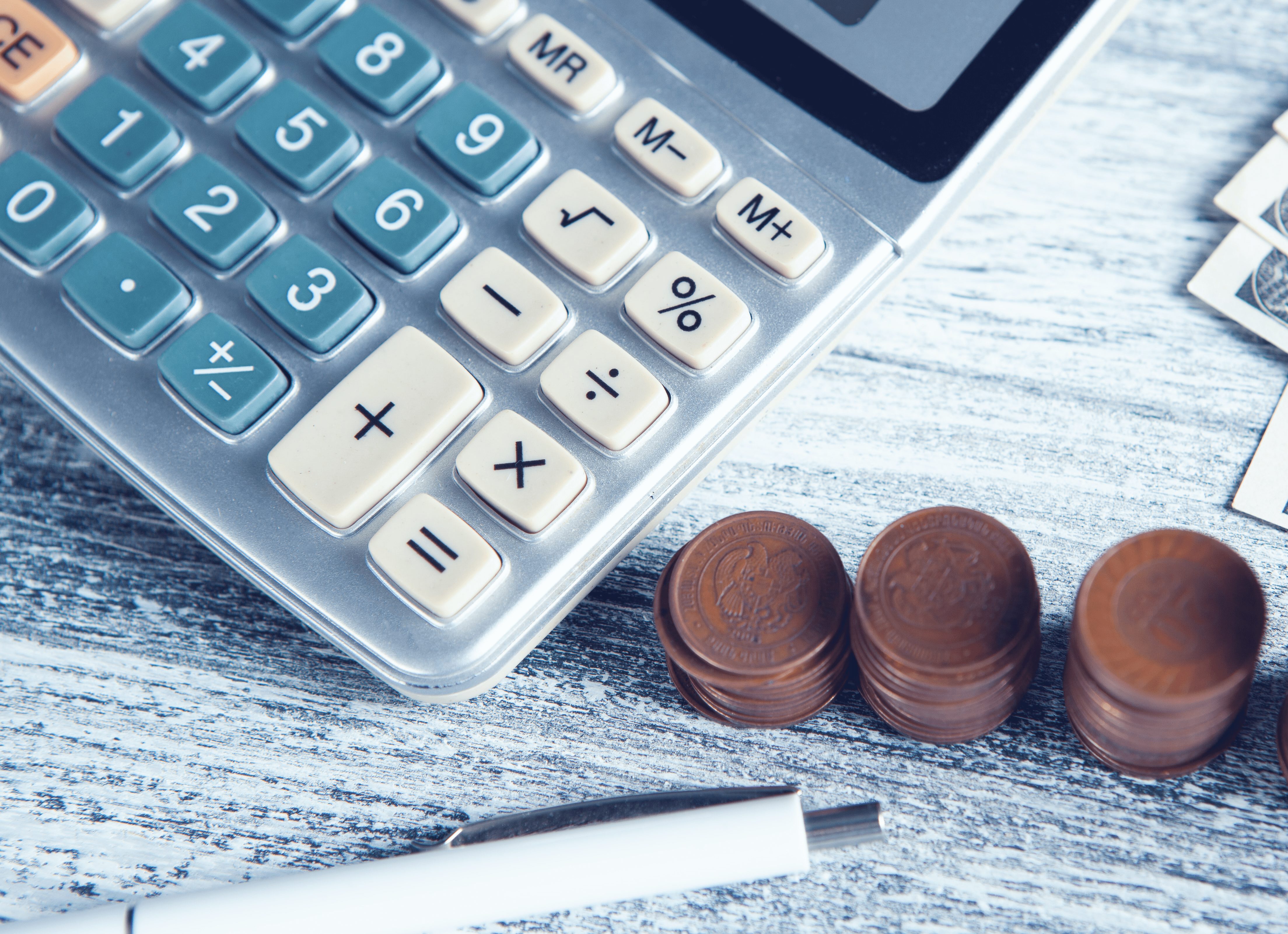 Foto de calculadora ao lado de moedas e uma caneta.