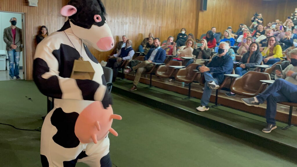 Foto de pessoa fantasiada de vaca em frente ao público em um auditório.