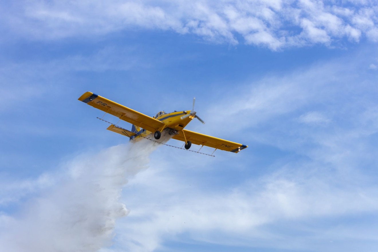 Foto de aviação agrícola sobrevoando e realizando a pulverização.