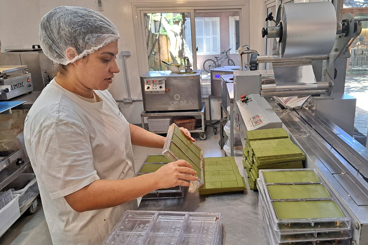Foto de mulher com EPI em fábrica realizando a produção de chocolate branco com erva-mate.