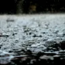 Foto de chuva caindo sobre poça de água.