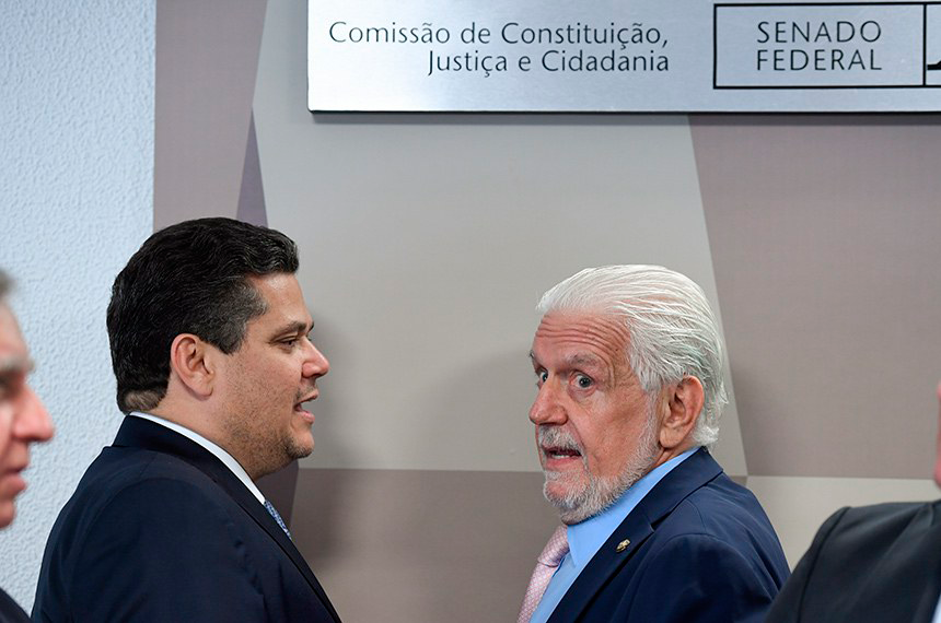 A foto mostra o O presidente da CCJ, Davi Alcolumbre, e o líder do governo no Senado, Jaques Wagner, conversando embaixo de placa que indica a