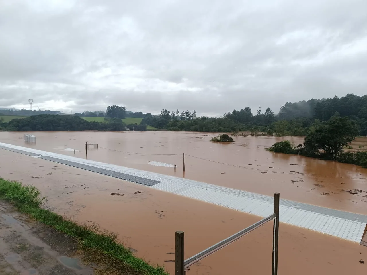 A foto mostra um local inundado. No centro aparece um telhado.