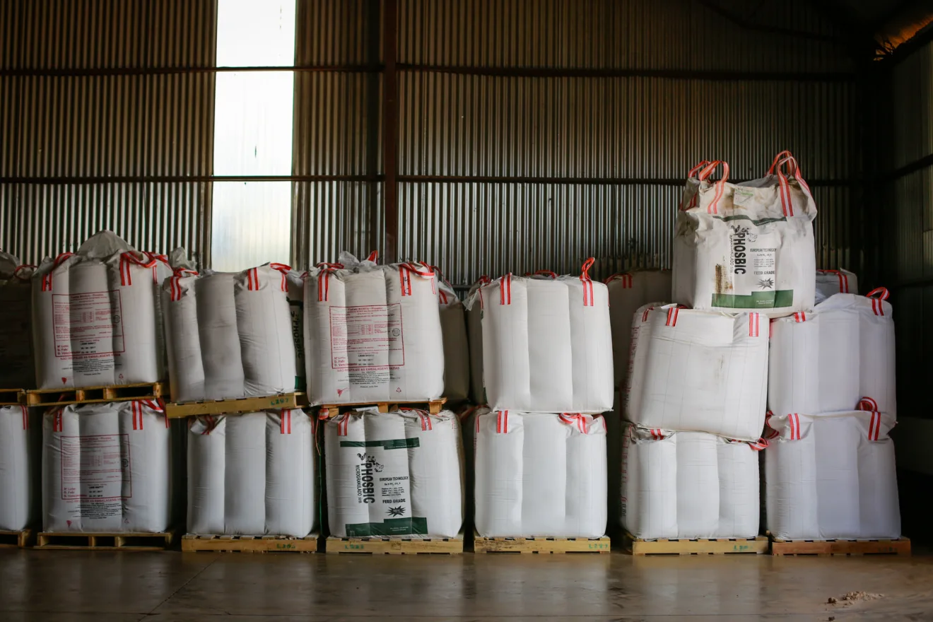 Foto de sacos de fertilizantes empilhados e enfileirados em galpão.