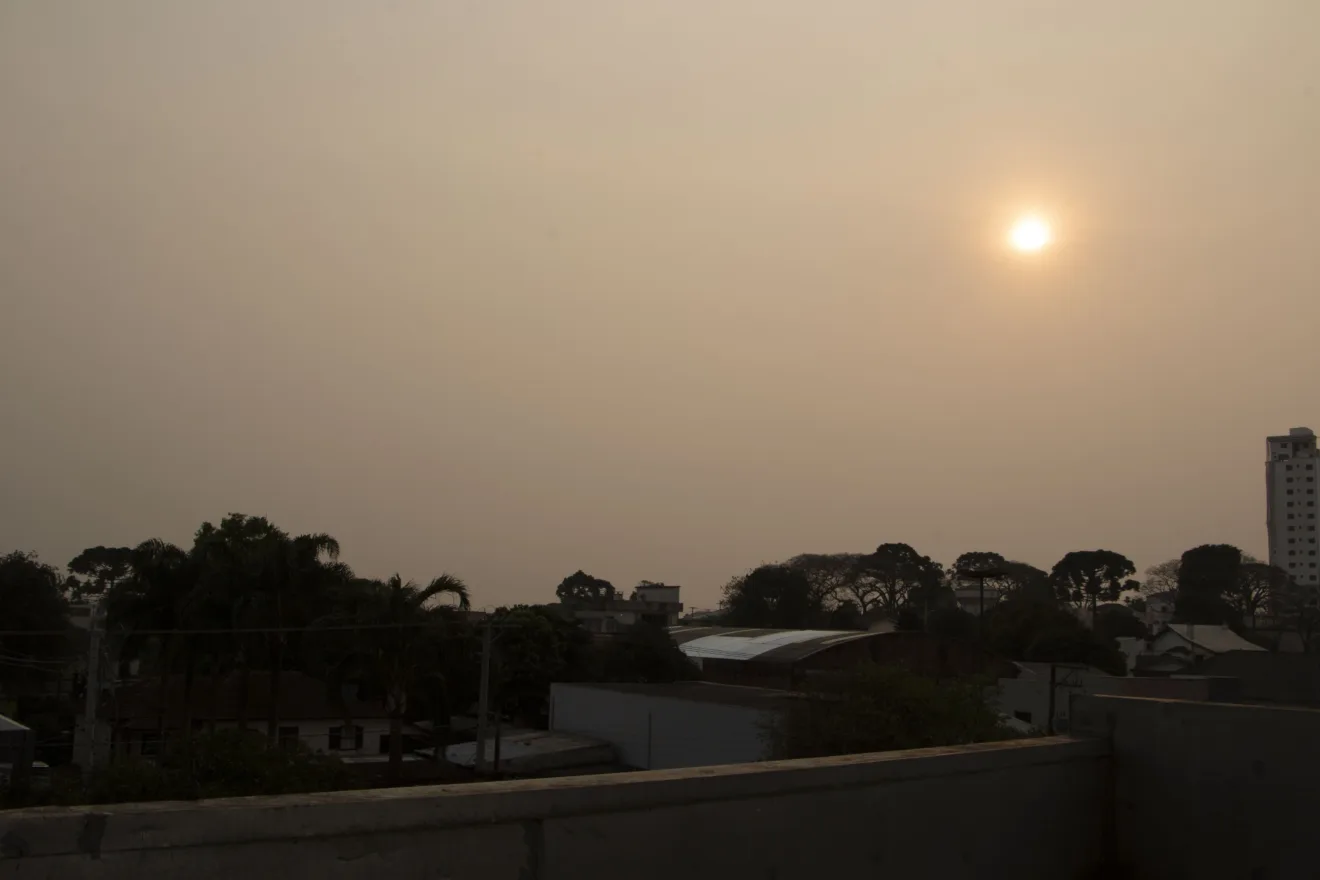 Foto de céu acizentado com sol avermelhado sobre cidade.