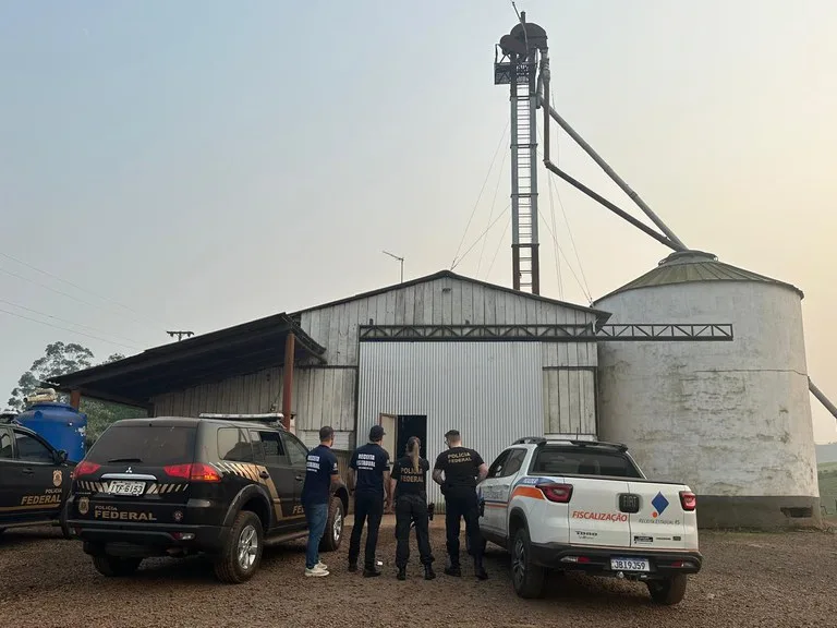 Foto de duas viaturas e quatro agentes em frente a silo.