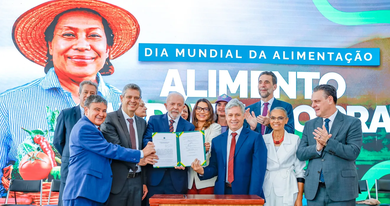Foto do Presidente da República, Luiz Inácio Lula da Silva cercado por ministros e outras pessoas segurando pasta aberta com decreto.