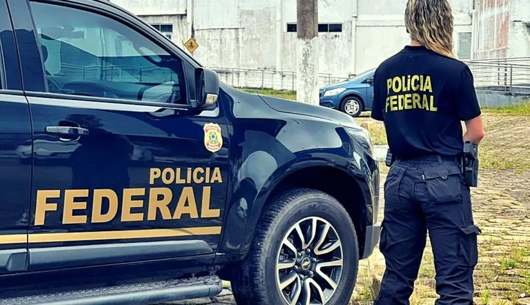 Foto de policial federal de costas ao lado de viatura.