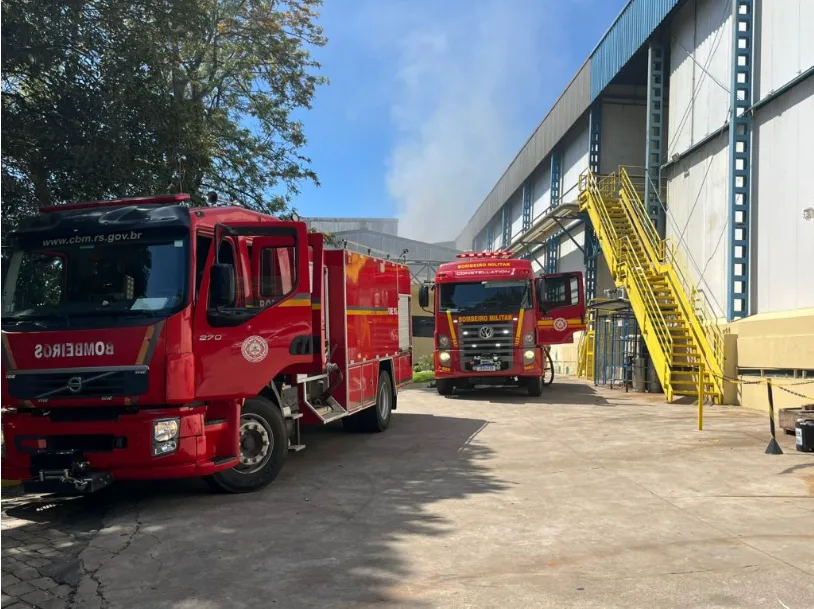 Foto de caminhões de bombeiros perto de unidade industrial e de fumaça.