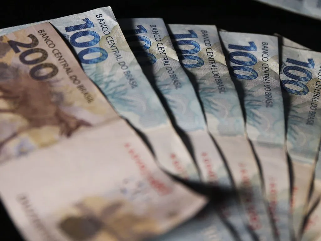 Foto de notas de cem e duzentos reais enfileiradas.