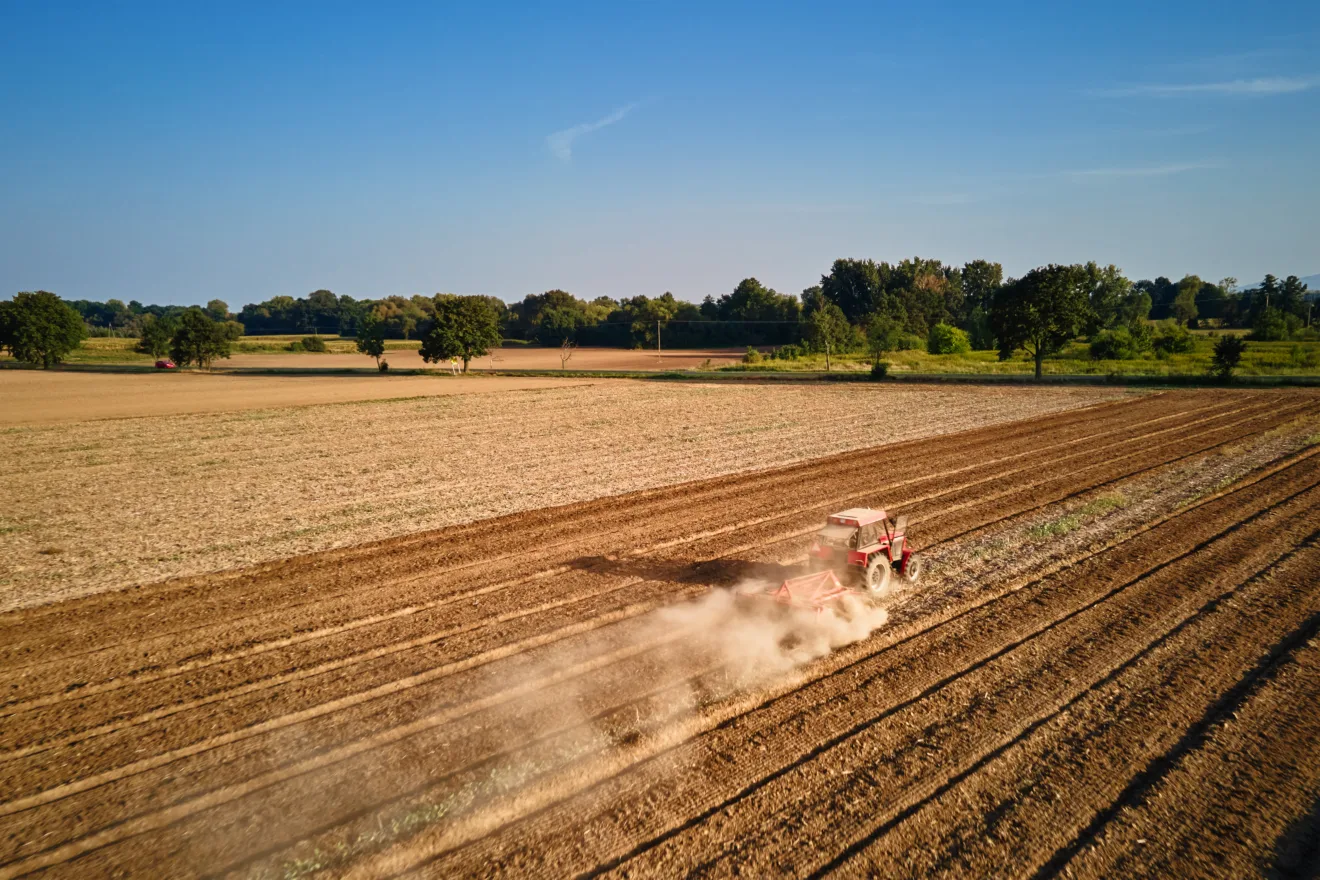 Trator trabalhando em campo agrícola, cultivando e arando solo seco.